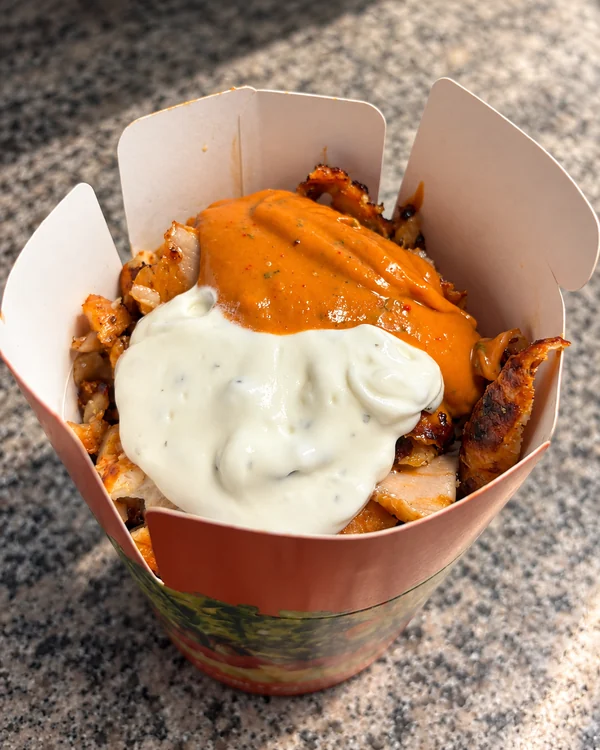 Geöffnete Döner Box mit Fleisch sowie weißer und orangefarbener Sauce