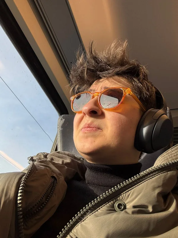 Eine Reisende mit Kopfhörern und orangefarbener Brille